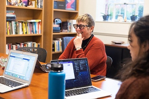 Carol Stabile at a table with students, talking and working on laptops