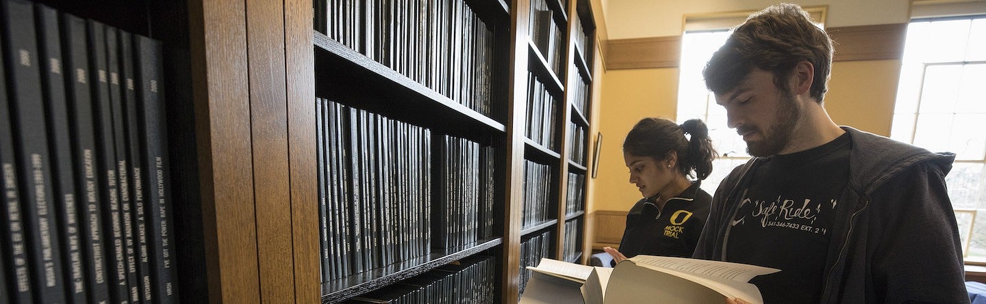 two students browsing a bookshelf of bound theses