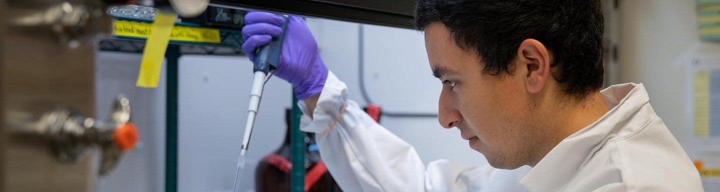 student nelson perez in lab coat using a pipette under a hood