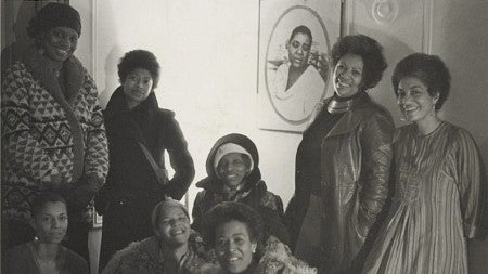 black and white photo of a group of black women gathered in a living room, smiling at camera
