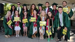 a group of students in graduation regalia, holding diplomas