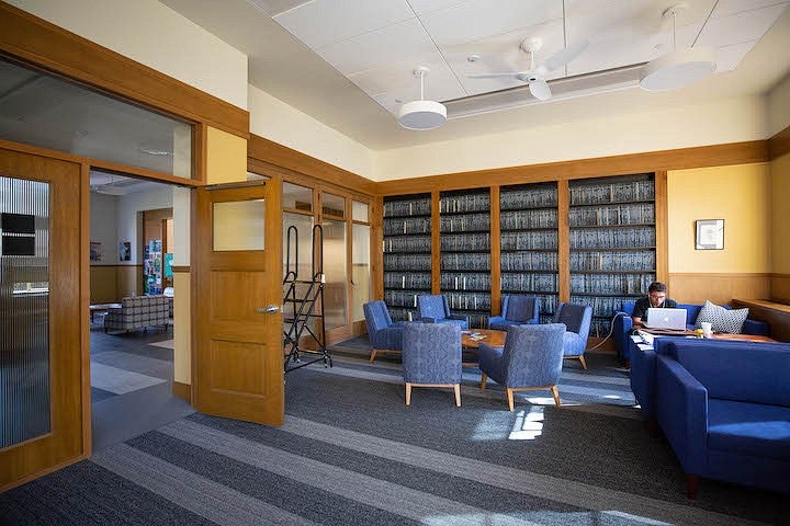 student working on laptop sitting on couch in front of shelves of theses in chapman hall library