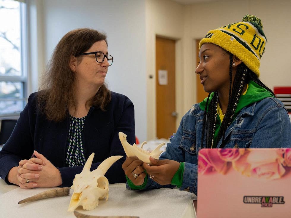 student (right) and faculty member (left) talking at table while looking at bone specimens
