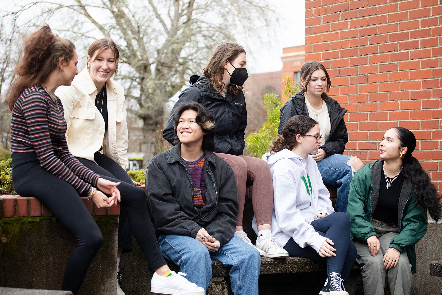 Students conversing outside a brick building in very early spring.