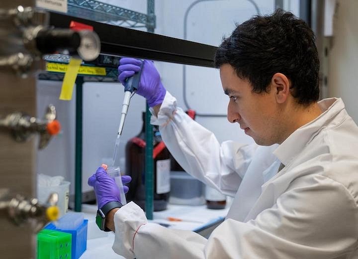 student in lab gear using pipette under fume hood