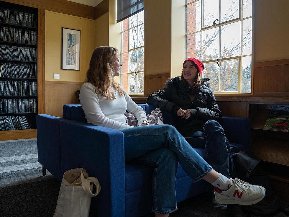 Two students seated on lounge chairs talking  