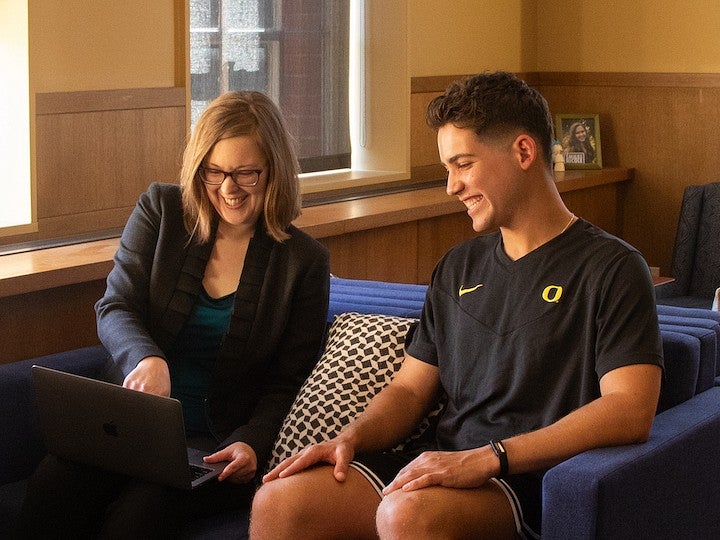 student and faculty member sitting on couch in honors library, smiling and looking at laptop