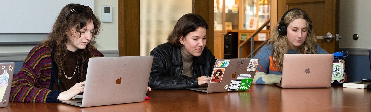 three students working independently on laptops at large table