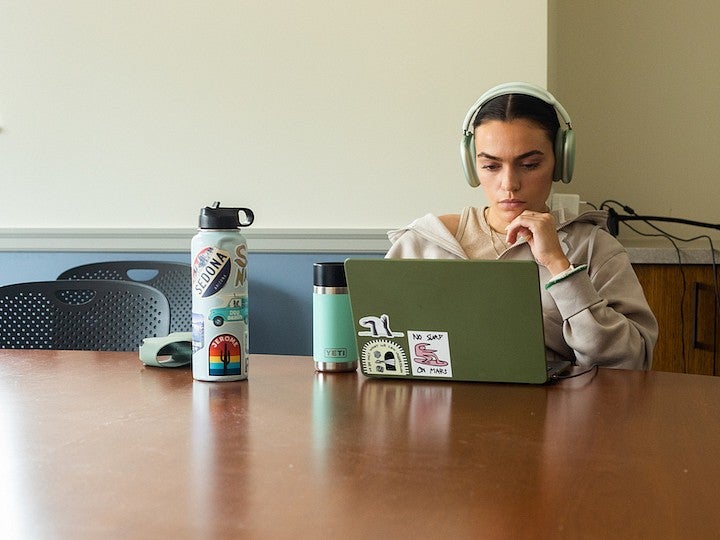 student working on laptop with headphones and waterbottle at large table