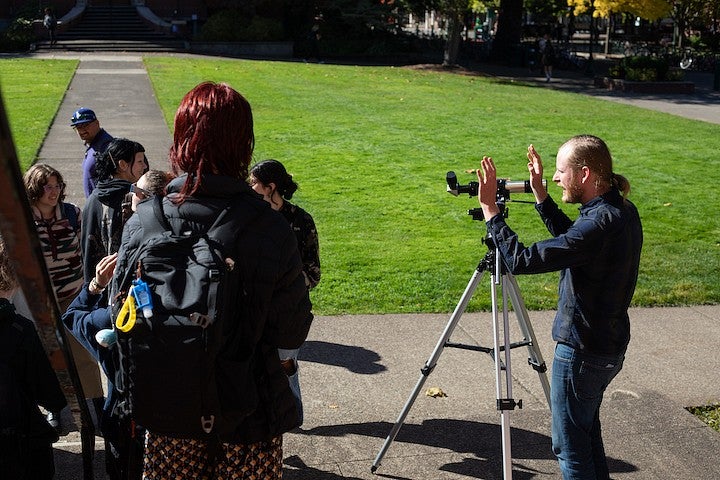 jesse feddersen teaching on the steps of chapman hall with a telescope and students sitting around