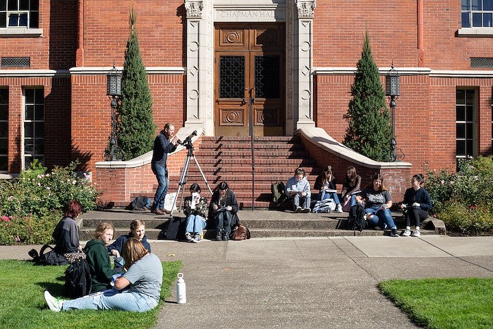 jesse feddersen teaching on the steps of chapman hall with a telescope and students sitting around