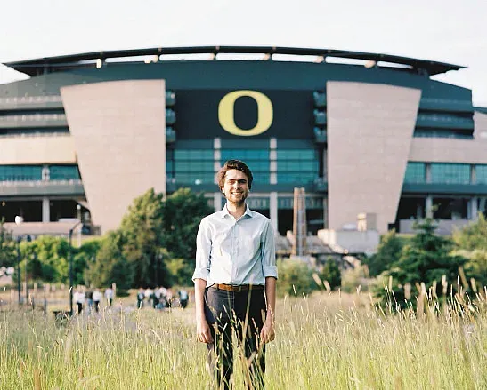 alum jakob hollenbeck standing in a meadow with autzen stadium in background