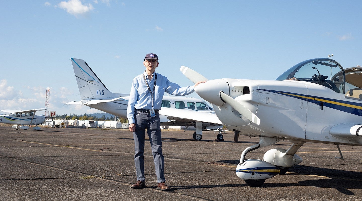robert mauro posing next to small plane on runway, wearing NASA cap