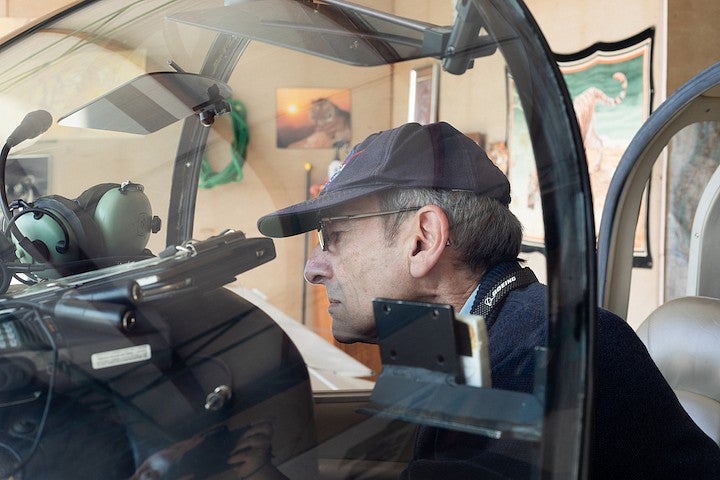 robert mauro taking a close look inside the cockpit of a small plane parked in a hangar with posters on the wall