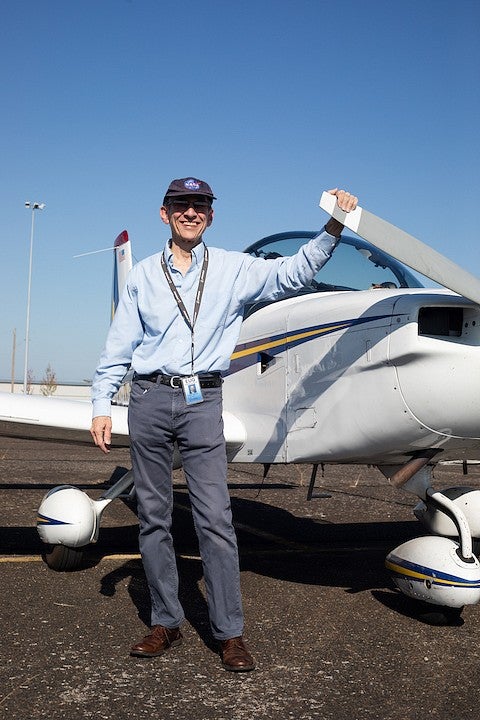 robert mauro posing with his small plane on the runway, wearing a NASA hat