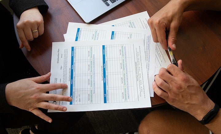 advisor and advisee's hands on a tabletop, working on filling out graduation plan form