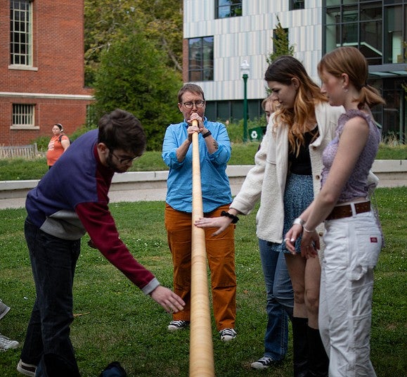 lydia van dreel playing the alpenhorn on tykeson lawn with students looking on