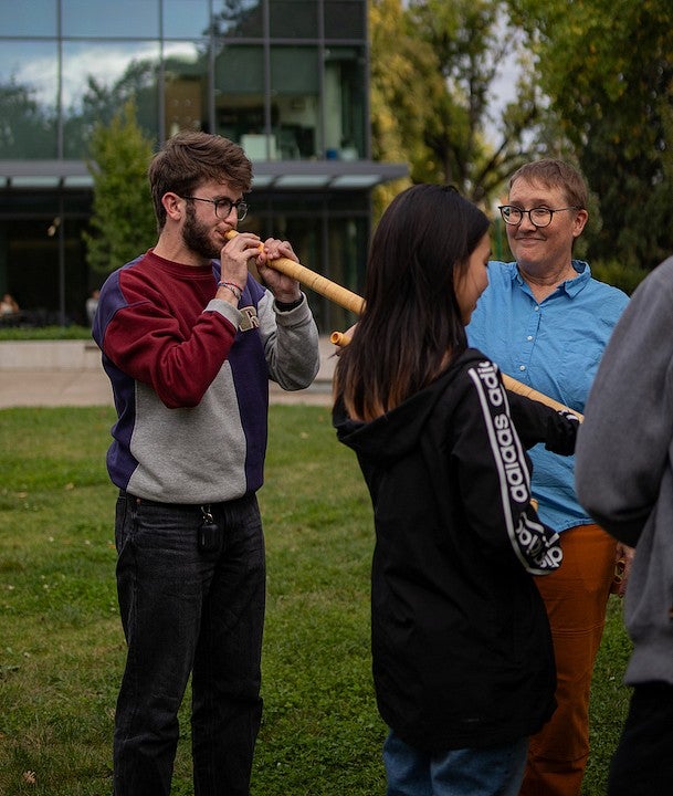 student plays alpenhorn on tykeson lawn while lydia van dreel looks on