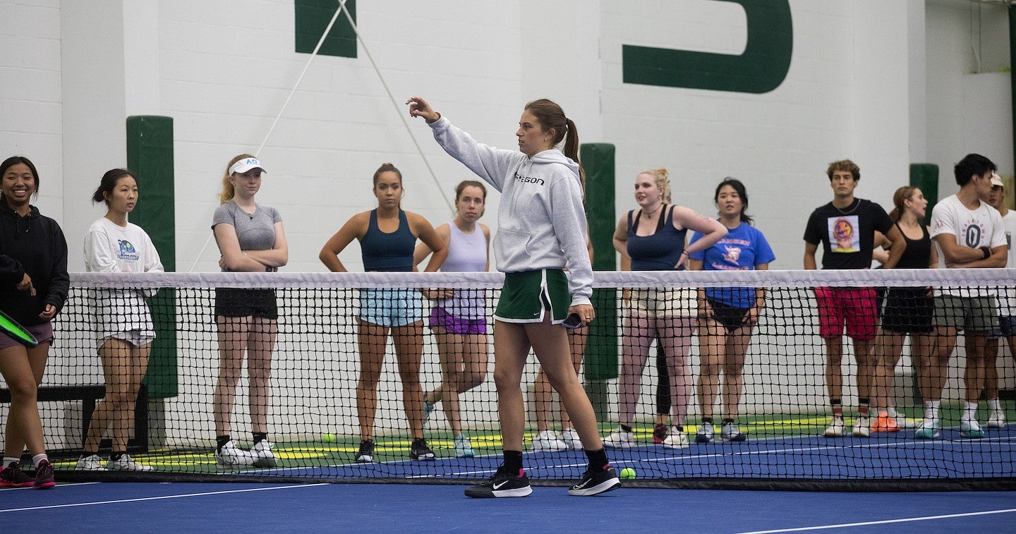ruby wool speaking to a group of tennis players on an indoor court