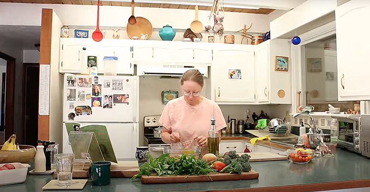 Elin England standing at her kitchen counter prepping vegetables with cooking implements hanging over her head