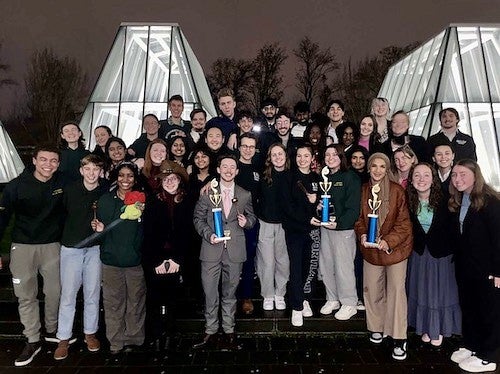 group of students posing with trophies outside building at night