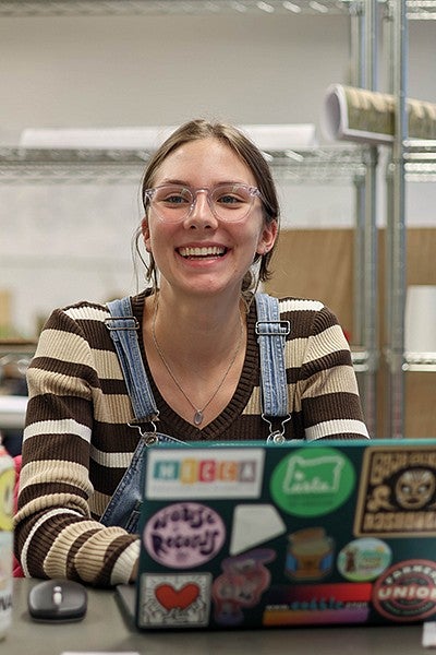 mia owen sitting at laptop in studio, smiling and laughing at someone off camera