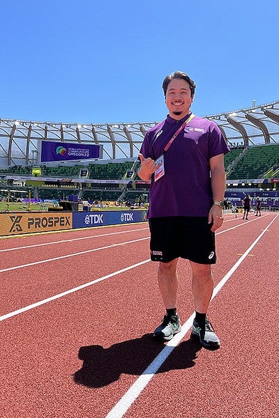 ryan horiuchi standing on hayward field track on sunny day wearing world athletics championships staff shirt