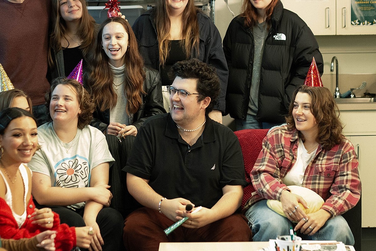 group of student journalists smiling at a different camera, sitting together in a newsroom