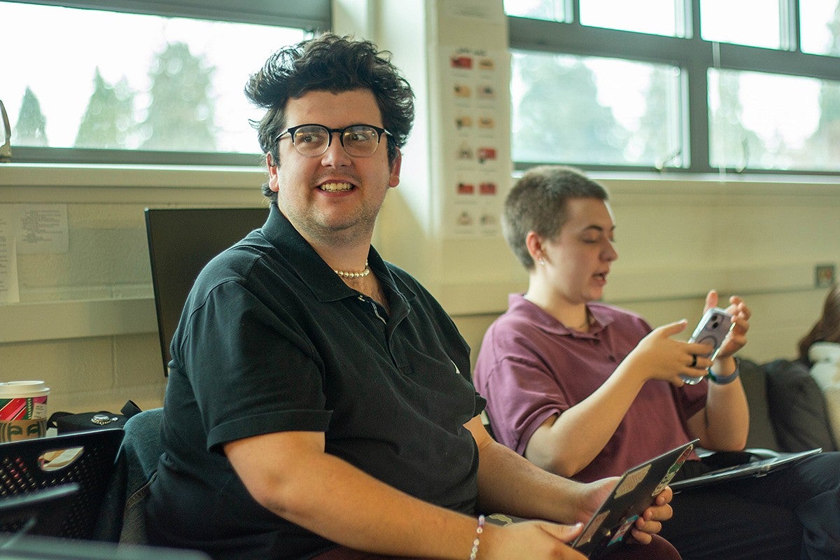 student editor in chief evan reynolds in the daily emerald news meeting, seated, glancing over shoulder and smiling