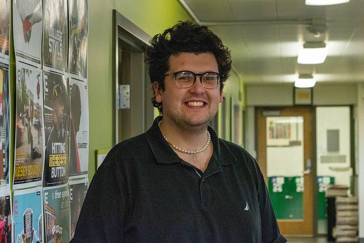 portrait of evan reynolds in hallway with daily emerald newspaper front pages covering the wall behind him