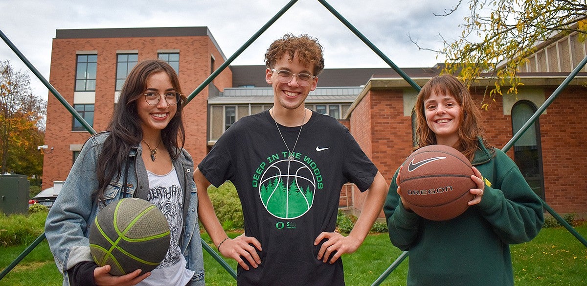 three student leaders of the firegen collaborative pose under an outdoor basketball hoop on the UO campus