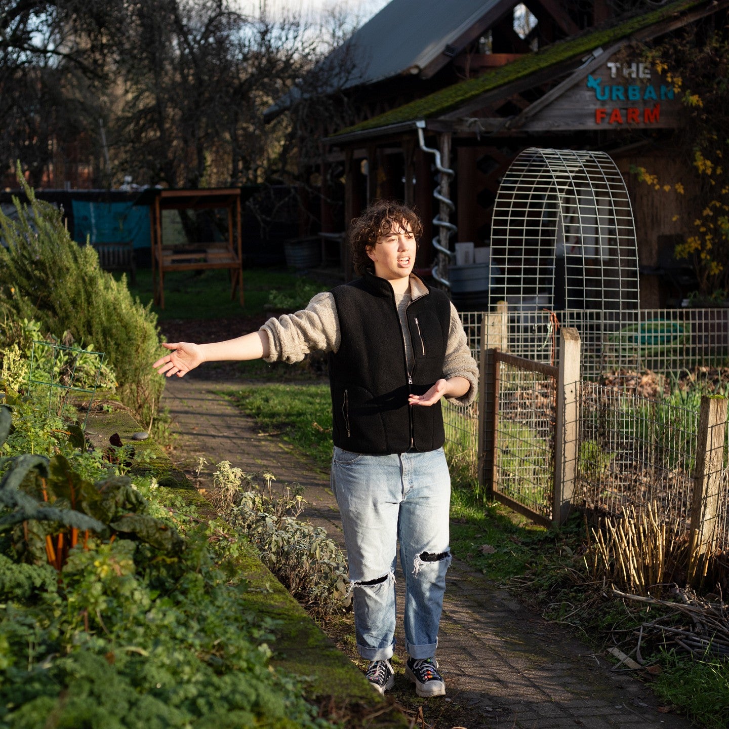 student teddy clayton gestures toward a plant bed as he talks about what's growing at the Urban Farm on a sunny winter day