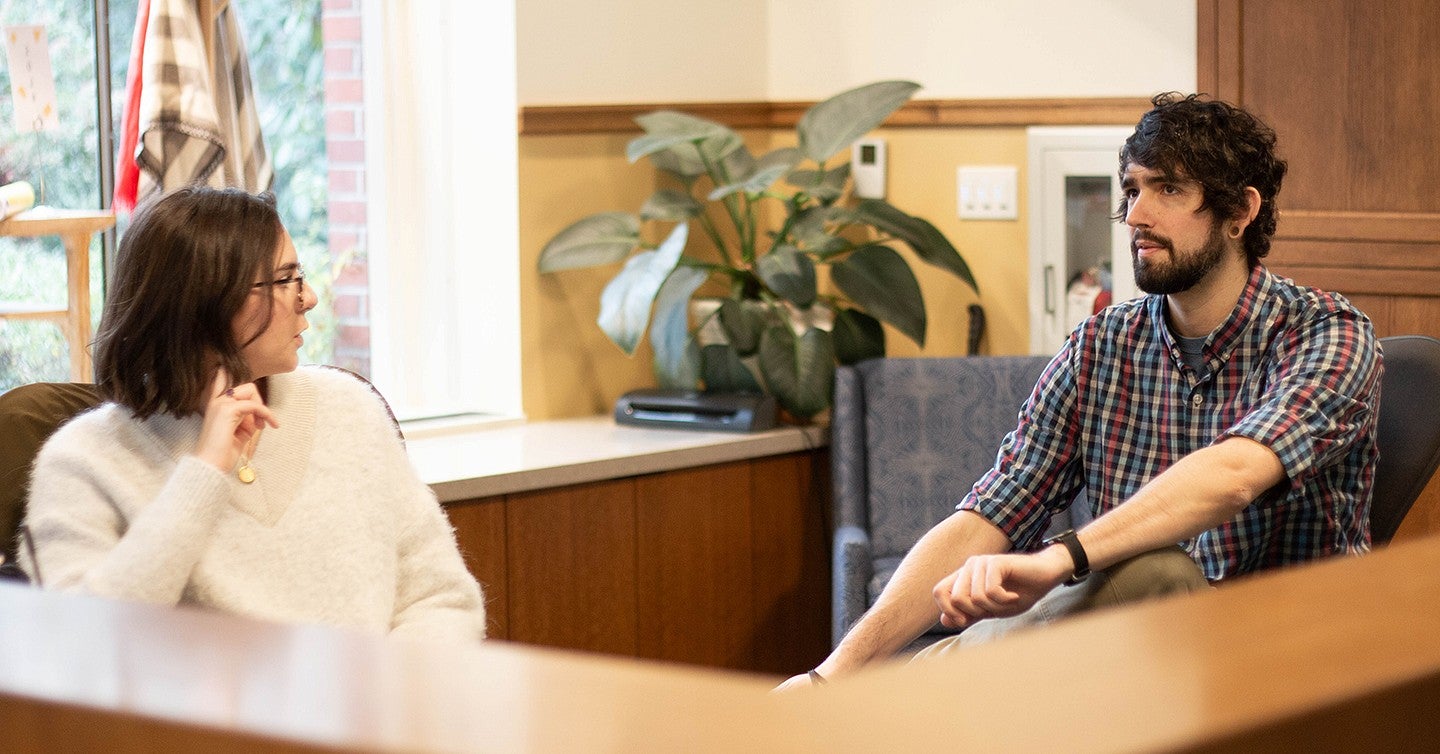 a student and a staffperson, Ryan Theiss, sitting behind the Chapman Hall reception desk, talking