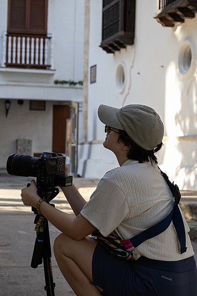 person crouching in courtyard with video camera on monopod, looking up at buildings
