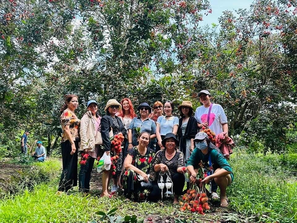 a group of Vietnamese women standing together under rambutan trees, posing with the red fruits