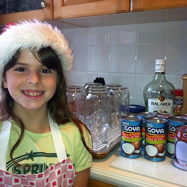 young girl in kitchen with santa hat and apron, standing in front of kitchen counter with canned coconut milk and rum