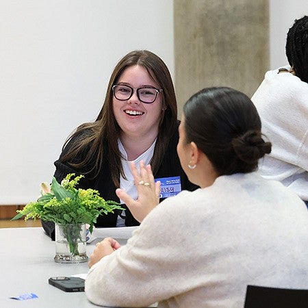 two students seated across a table from one another, talking