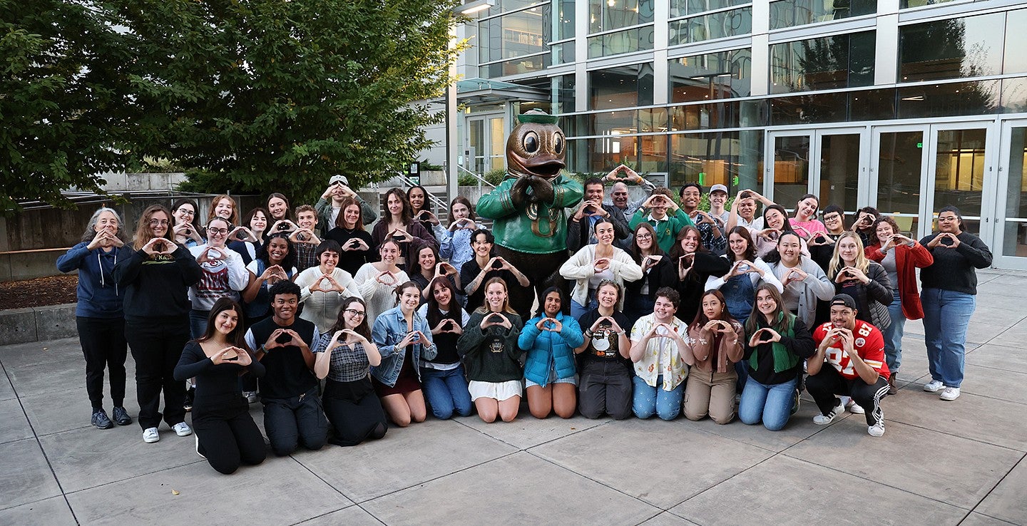 group of students clustered around the duck statue on UO campus, throwing the O