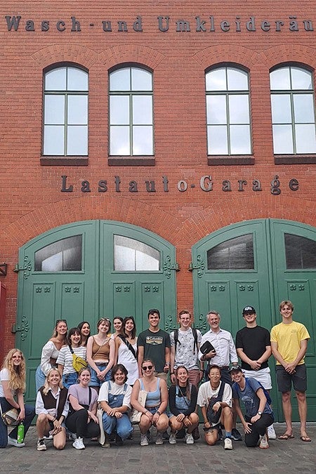 group of students posing outside brick building with german words on it