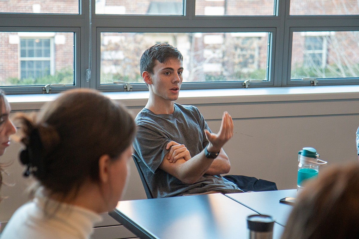 charlie petrik talking animatedly in a room seated around tables with other students