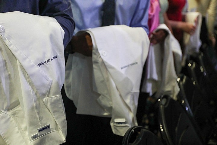 people with white medical coats embroidered with "school of medicine" draped over their arms