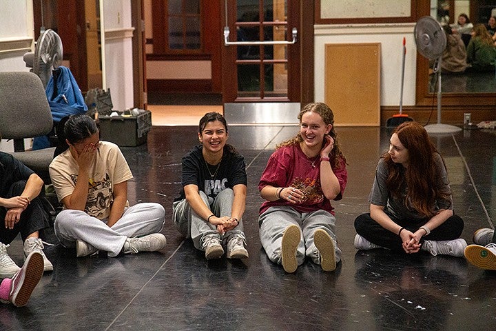 group of girls at dance practice seated on floor in semicircle, talking and laughing