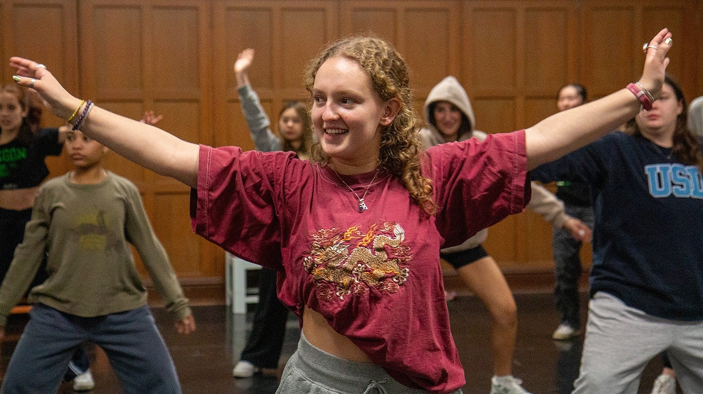 student sierra hawes at dance practice, spreading her arms wide and smiling along with other young women