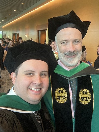robert cloutier and a student dressed in graduation regalia, posing for a selfie