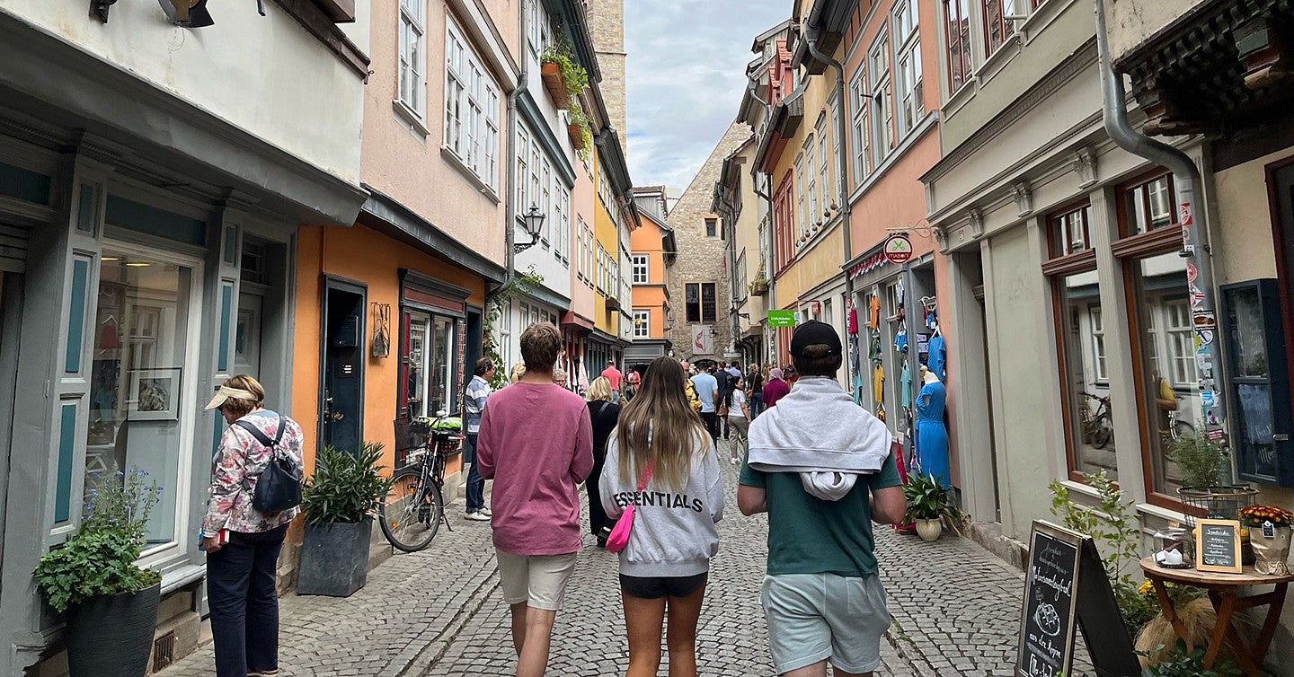 group of students walking down a narrow pedestrian cobblestone street with european buildings