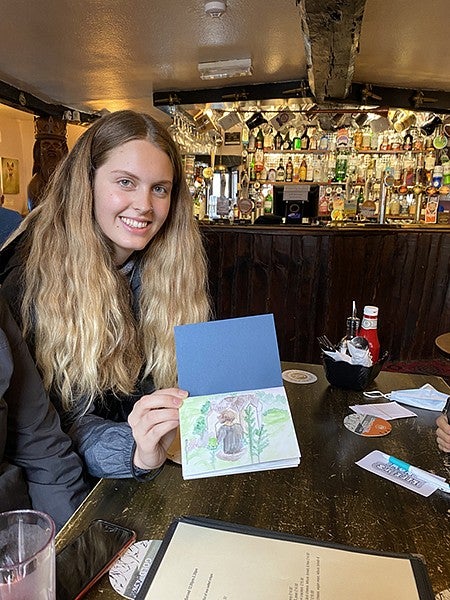girl showing page of sketchbook with drawing while sitting at pub table
