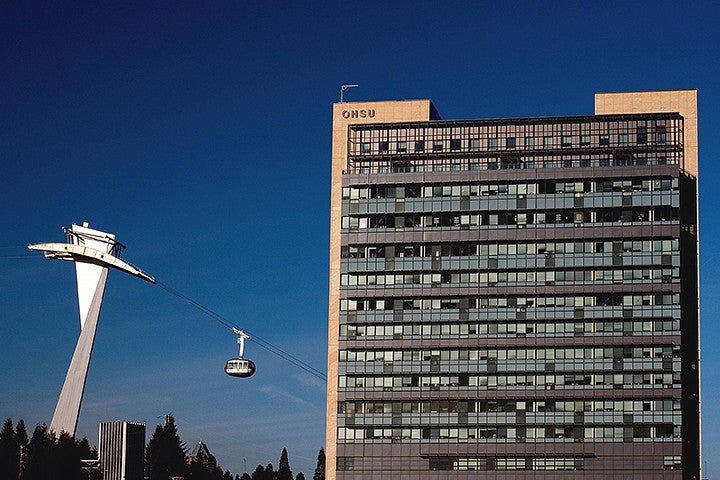 building with "OHSU" on side next to aerial tram operating on a sunny day
