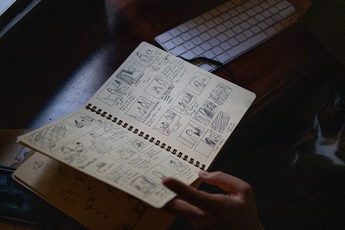 desktop with open sketchbook of comic panels in black ink