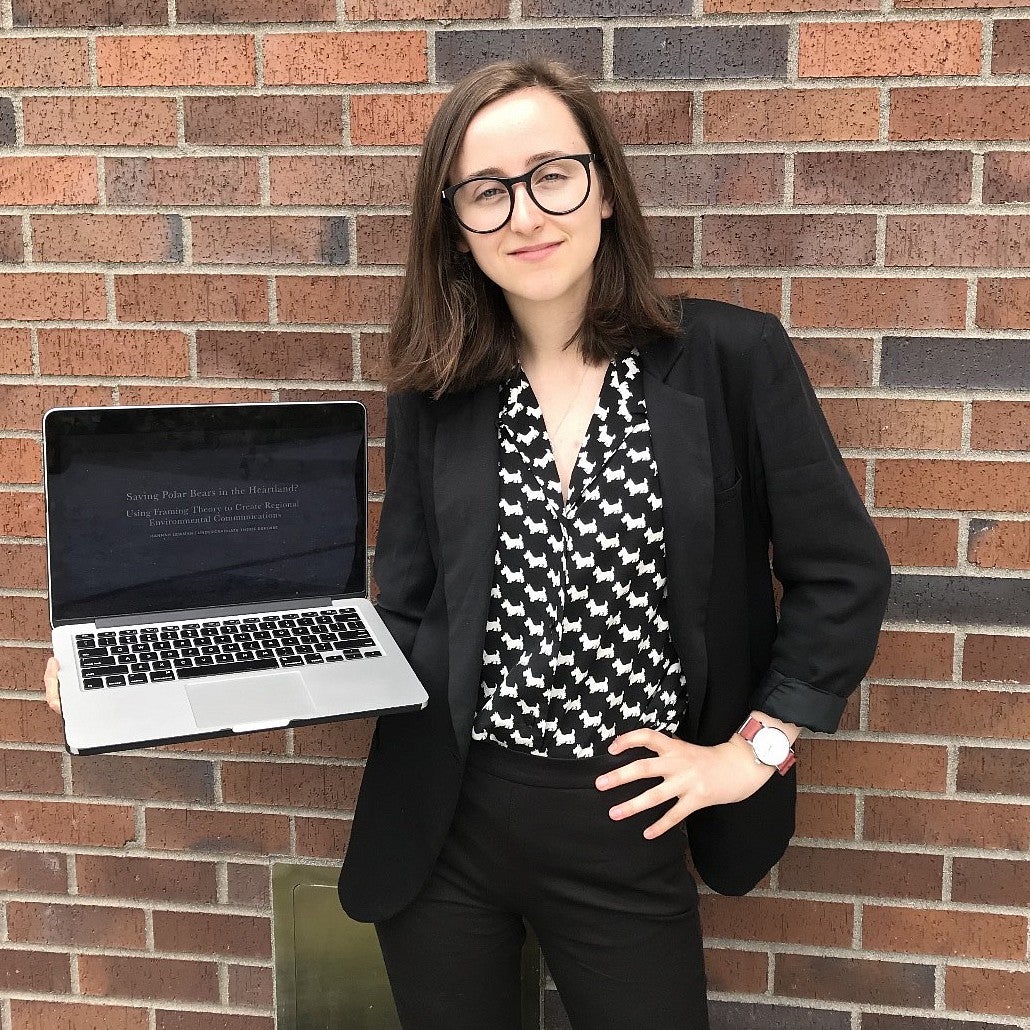 portrait of hannah lewman posing with laptop in front of brick wall