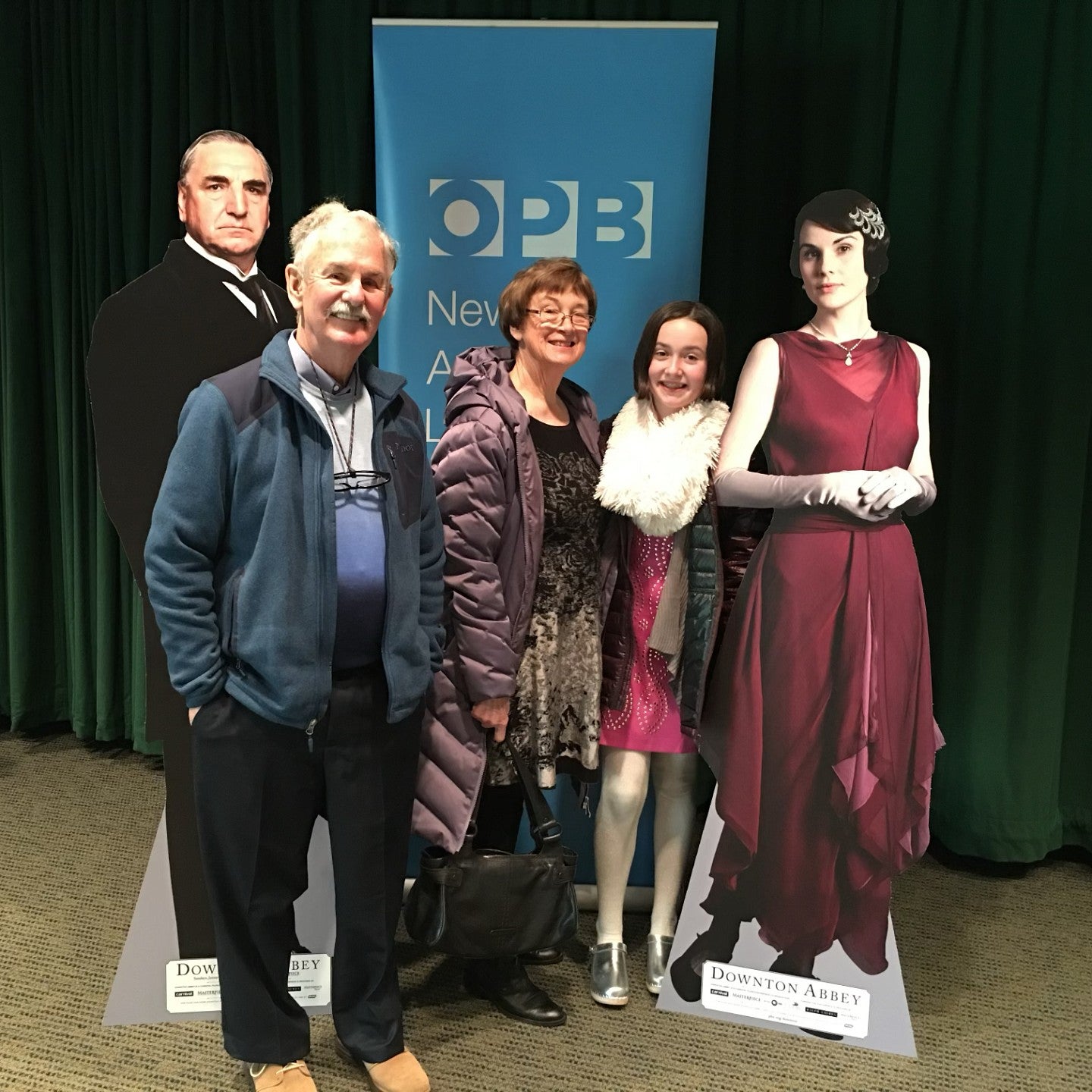 family posing in front of cardboard cutouts of Downton Abbey characters and a sign with OPB logo